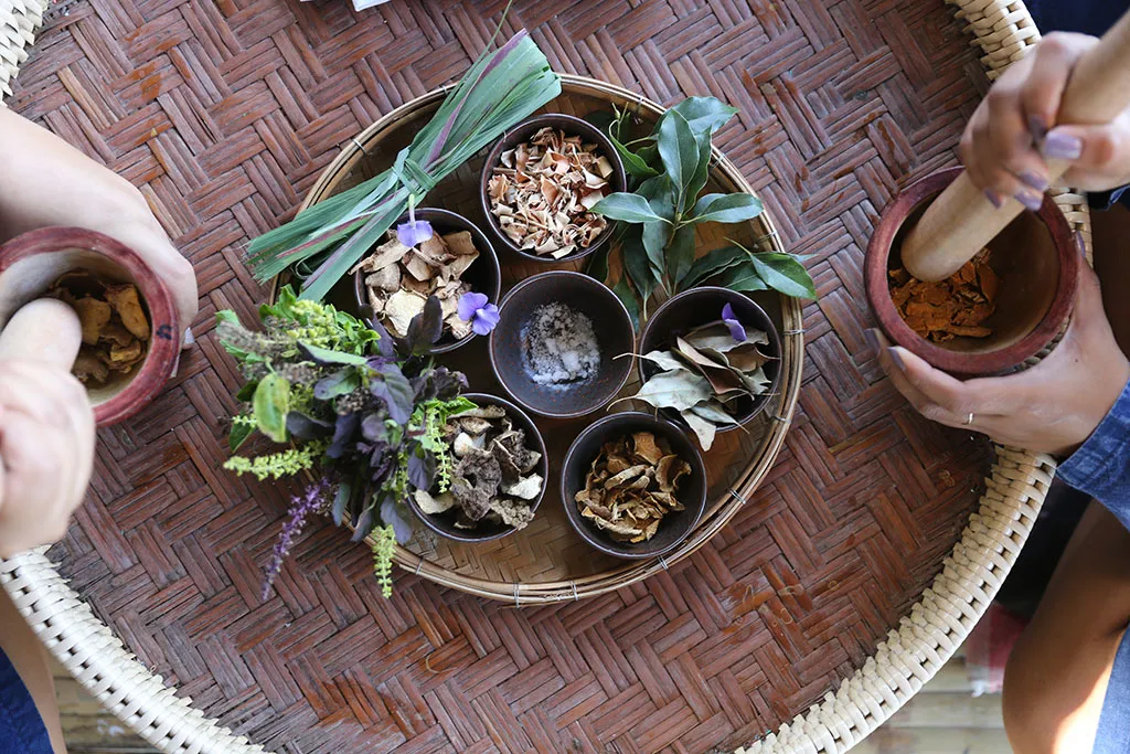Hands grinding Thai herbs to make a traditional herbal inhaler / มือกำลังบดและผสมสมุนไพรเพื่อทำยาดม